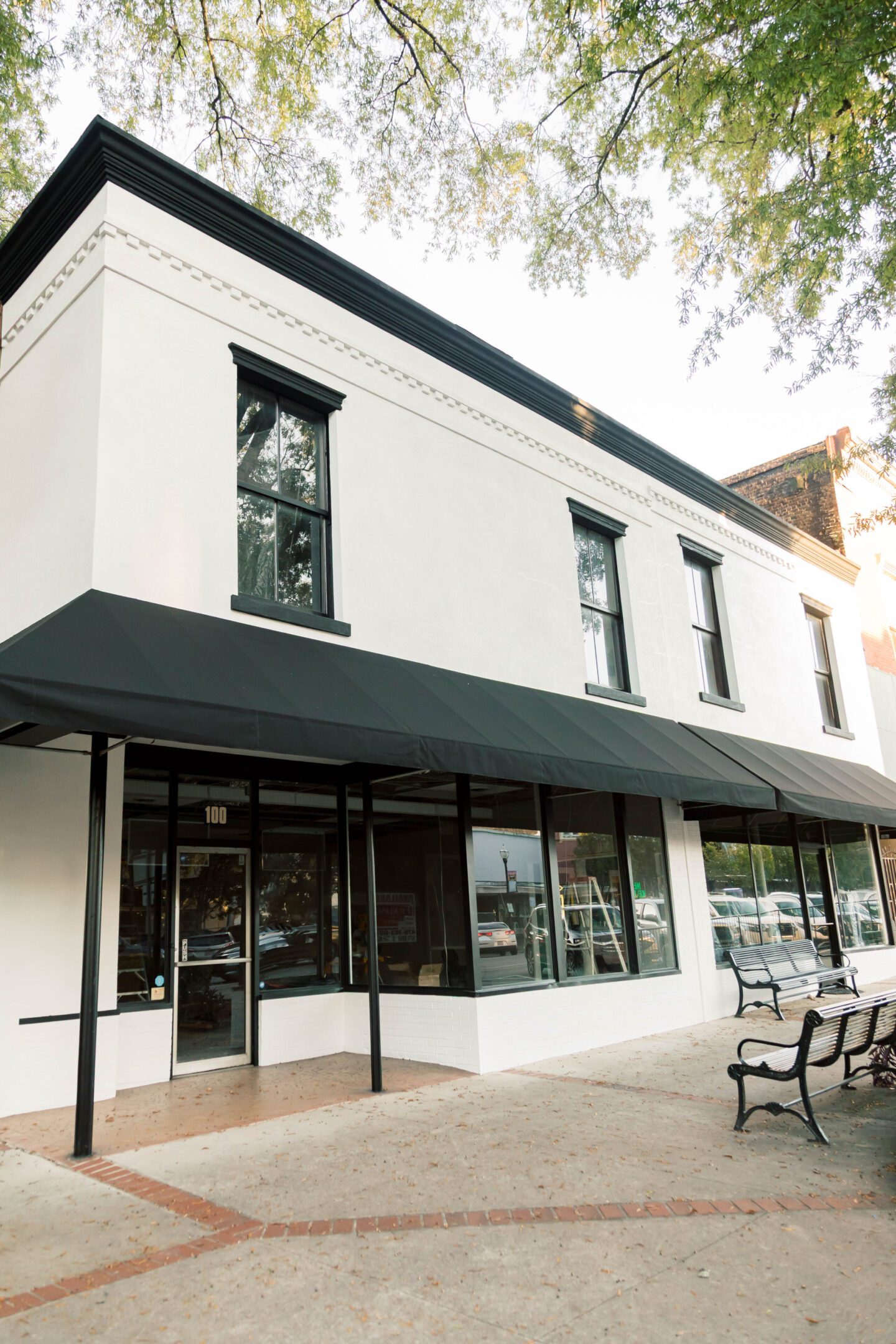 White two-story building with black awnings and glass storefront windows.